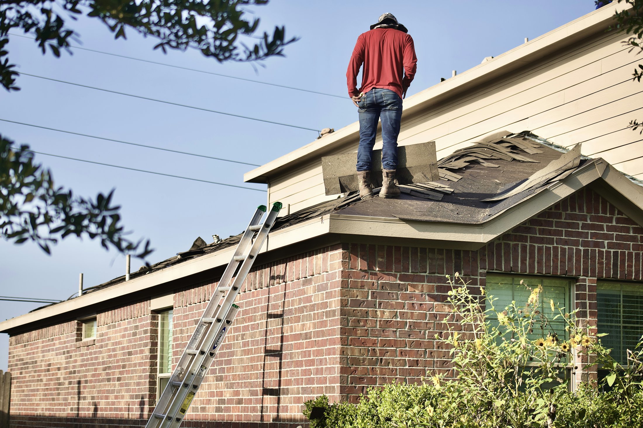 A Hammer Down roofer removing old shingles from a brick home ahead of a full roof replacement