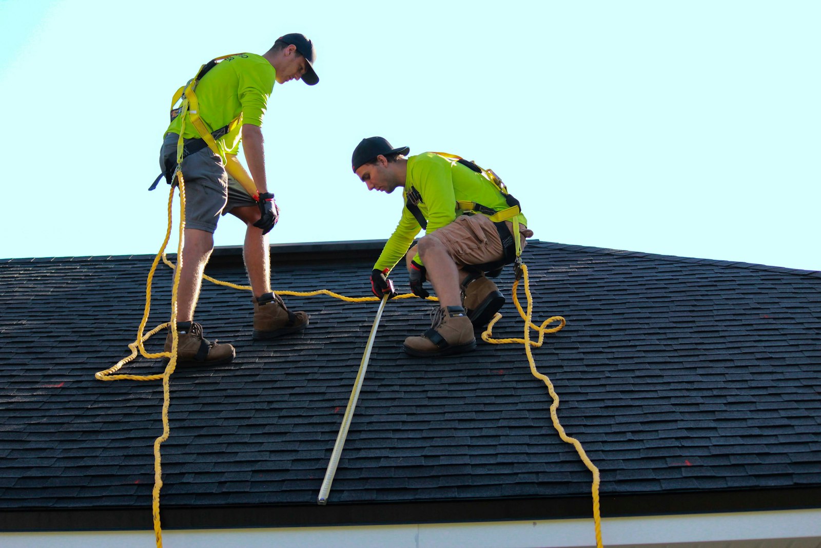 Two Hammer Down crew members in safety harnesses working on a shingle roof
