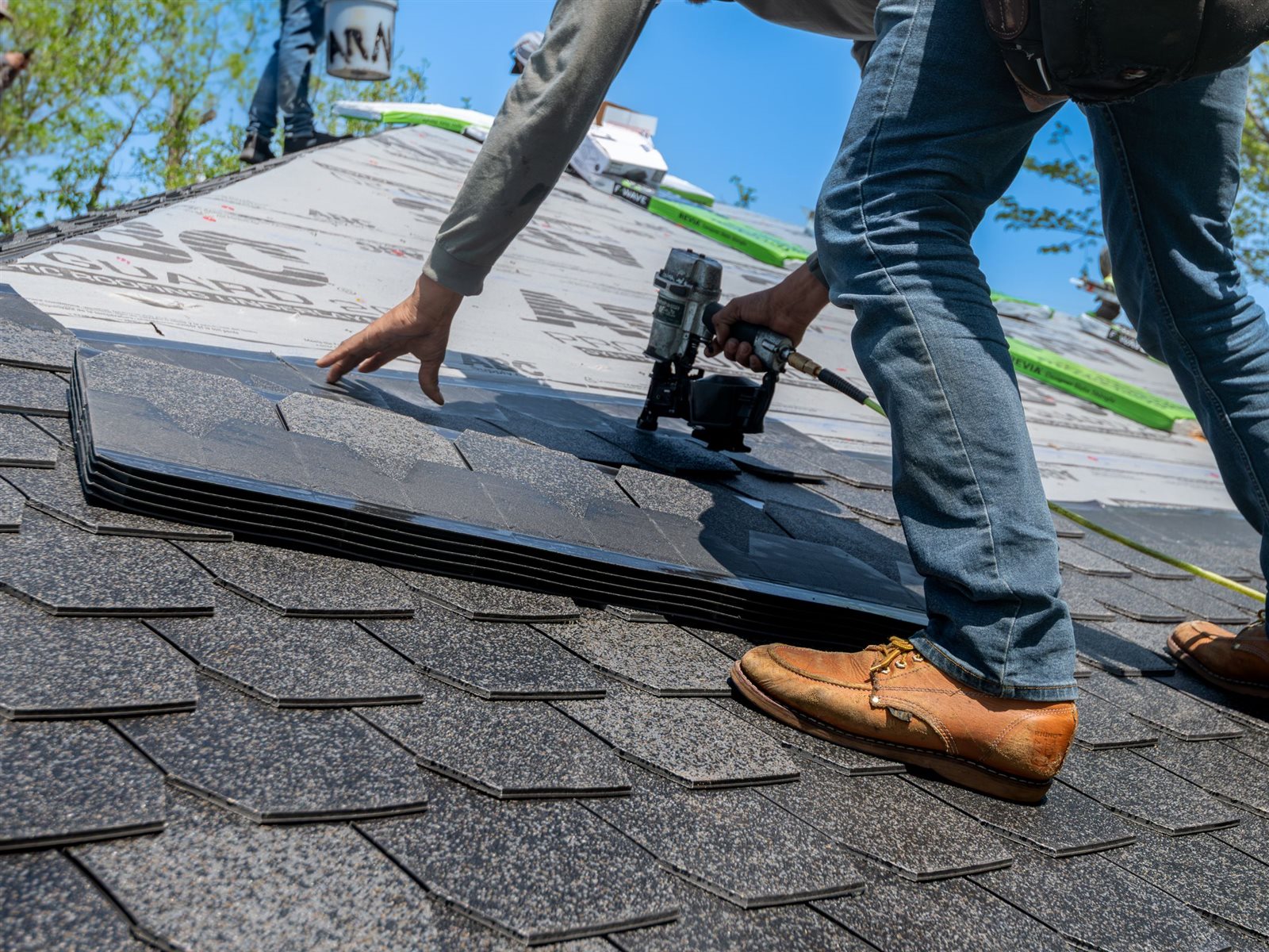 Roofer using a pneumatic nail gun to fasten an asphalt shingle during a roof repair