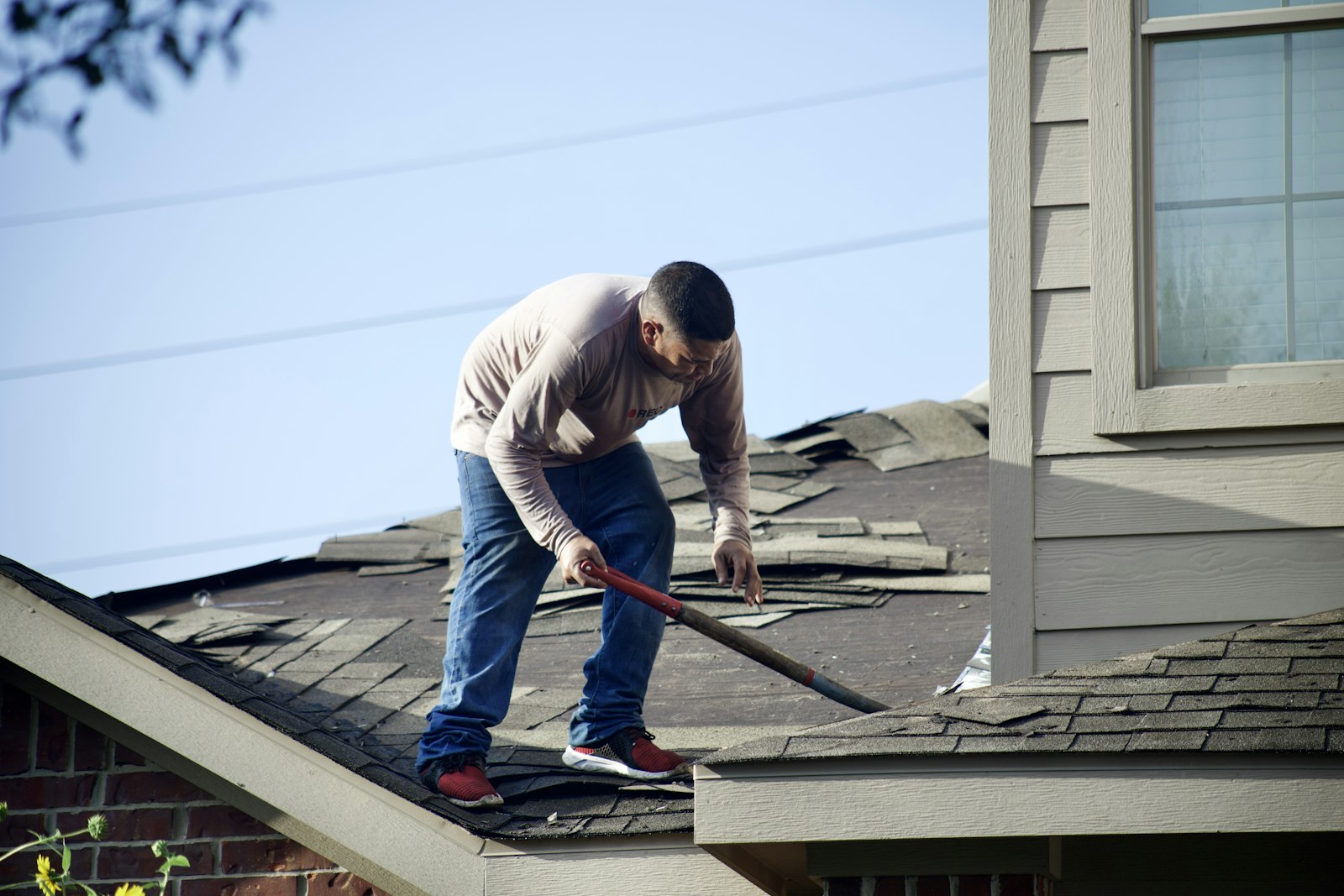 Roofer tearing off old shingles during a roof replacement